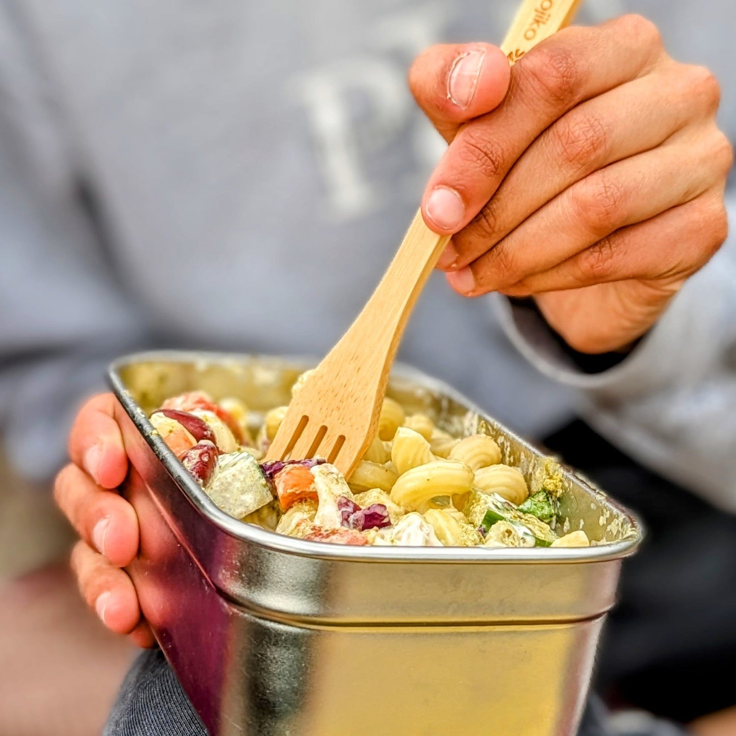 Van life meal: pasta salad in metal container with bamboo fork, perfect for camper van adventures and outdoor dining.
