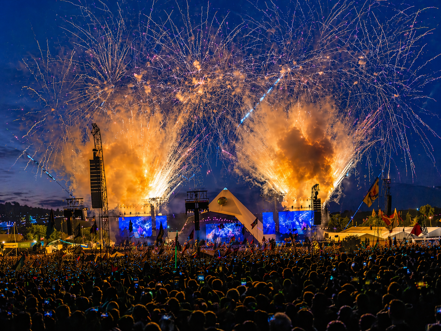 Large outdoor music festival at night with fireworks exploding above a packed crowd, glowing stage lights and energetic summer atmosphere, capturing the excitement of festival season, live music and outdoor adventure culture.