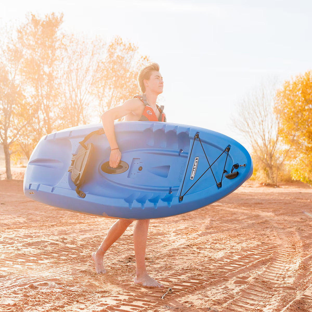 Man carrying blue kayak on sandy beach, perfect for van life adventures and outdoor exploration
