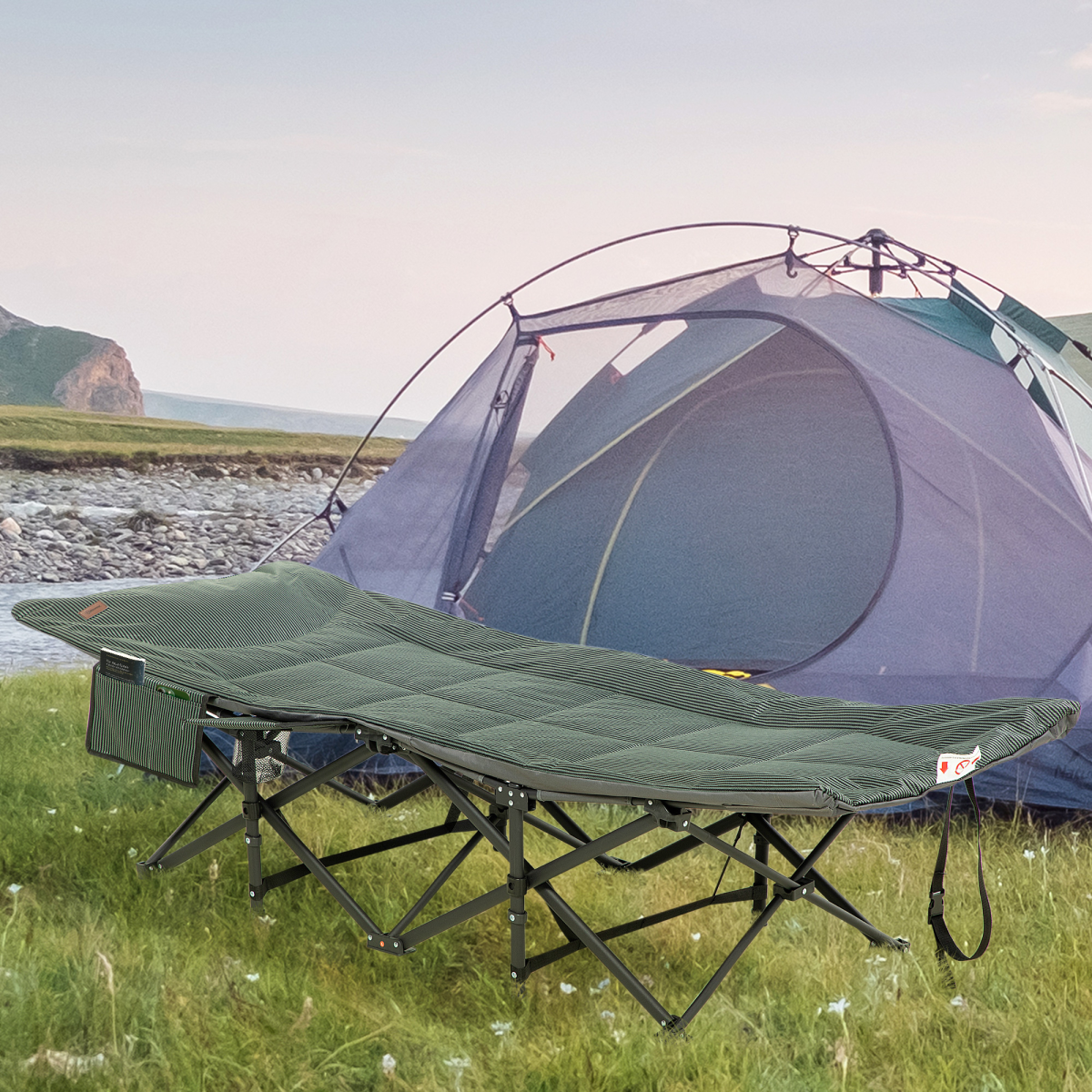 Portable camping cot with storage pocket beside tent on grassy field near river, ideal for van life and outdoor adventures