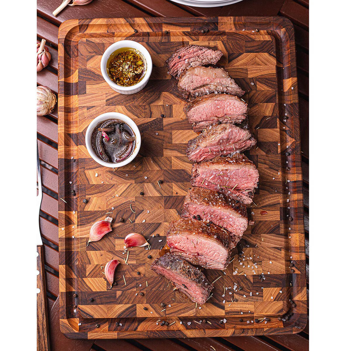 Sliced medium-rare steak on wooden cutting board with garlic, herbs, and dipping sauces for van life cooking