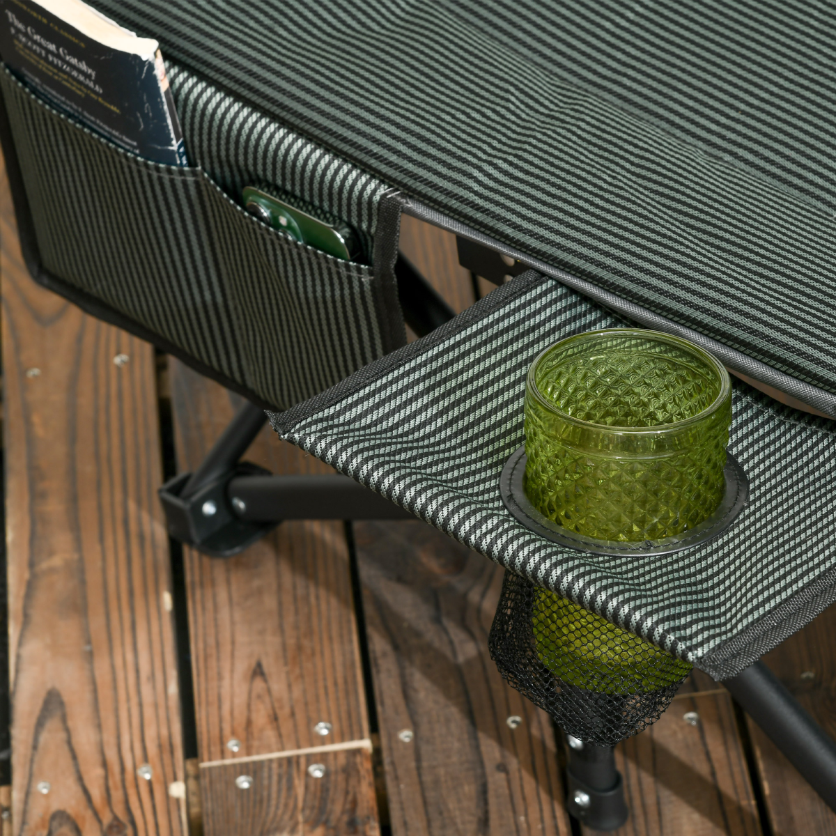 Striped camping chair with side pockets holding book, phone, and green glass in cup holder, ideal for van life adventures.