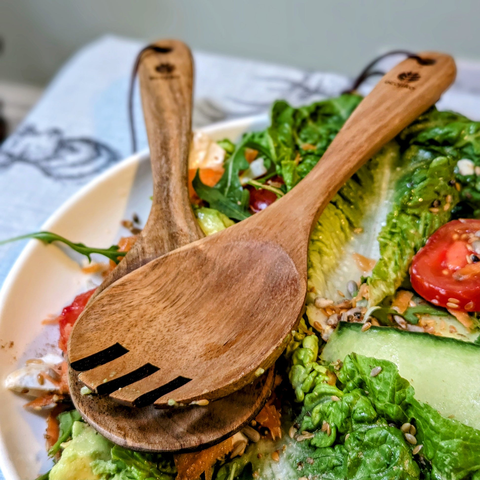 Wooden salad servers with engraved logo on fresh greens, perfect for van life camping meals and outdoor adventures.