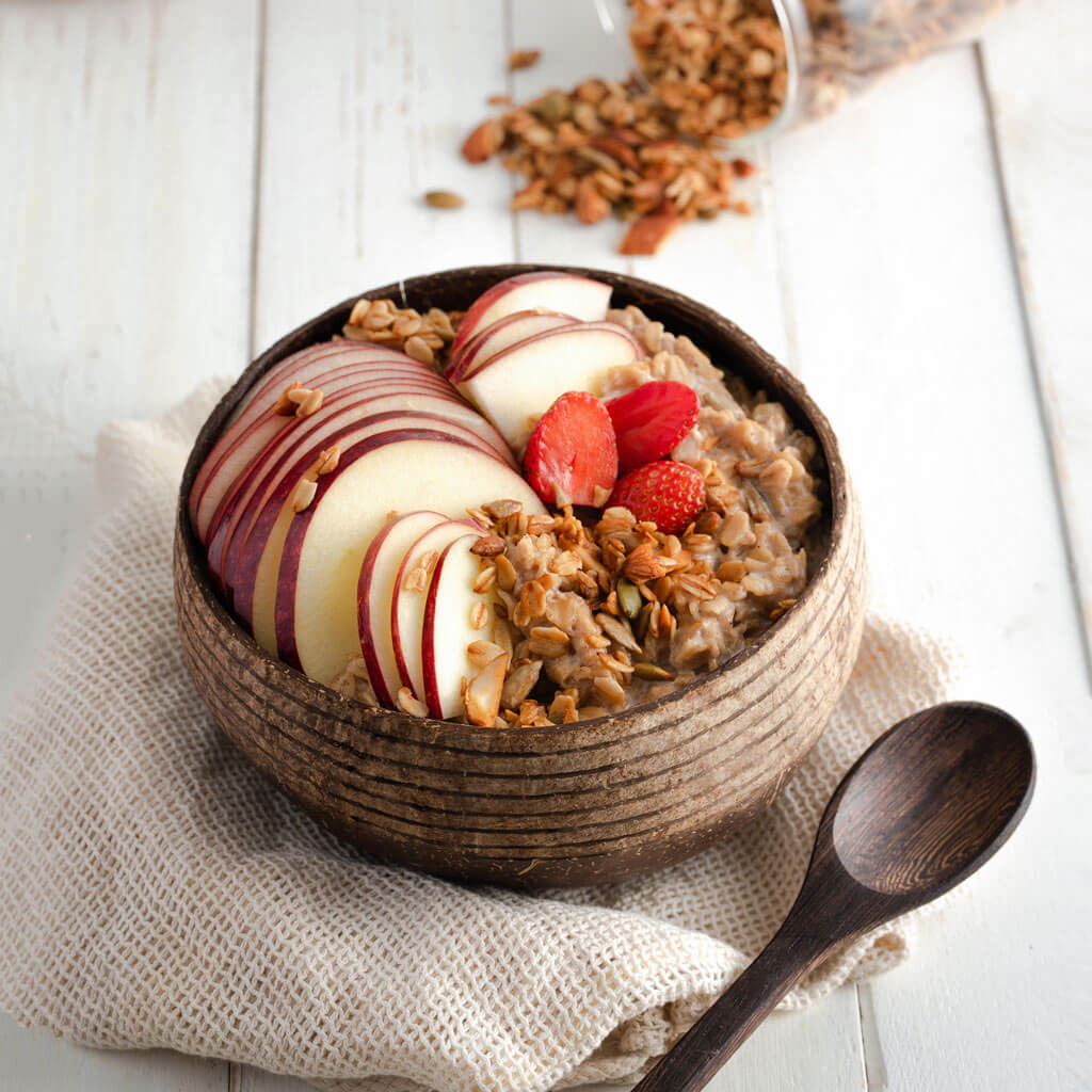 Coconut bowl with oatmeal, sliced apples, strawberries, and granola for van life breakfast