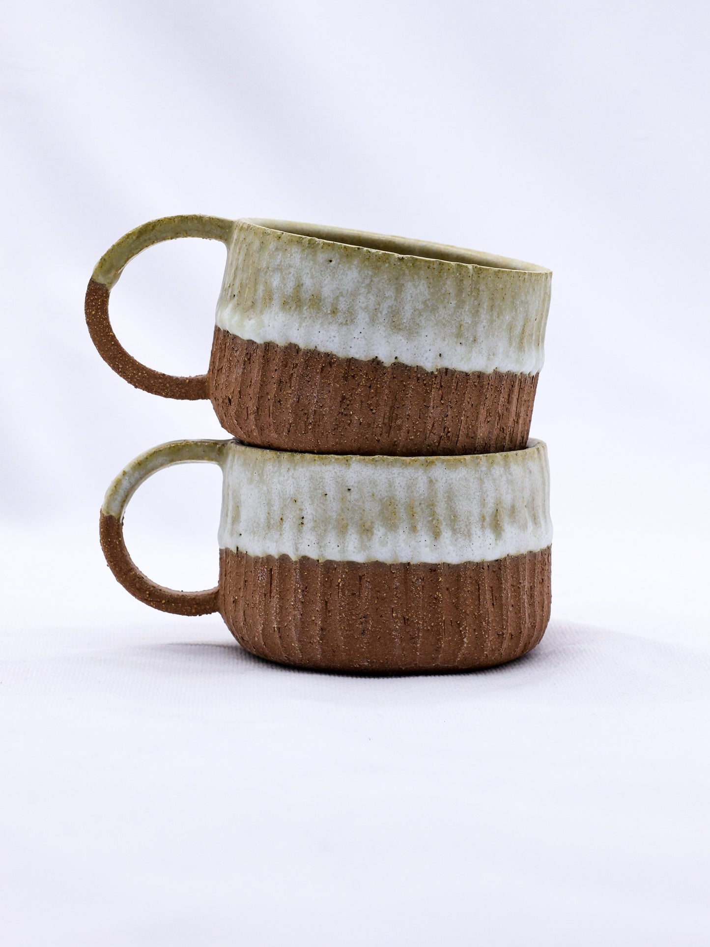 Stacked handmade ceramic mugs with ribbed texture, perfect for van life adventures and outdoor camping.