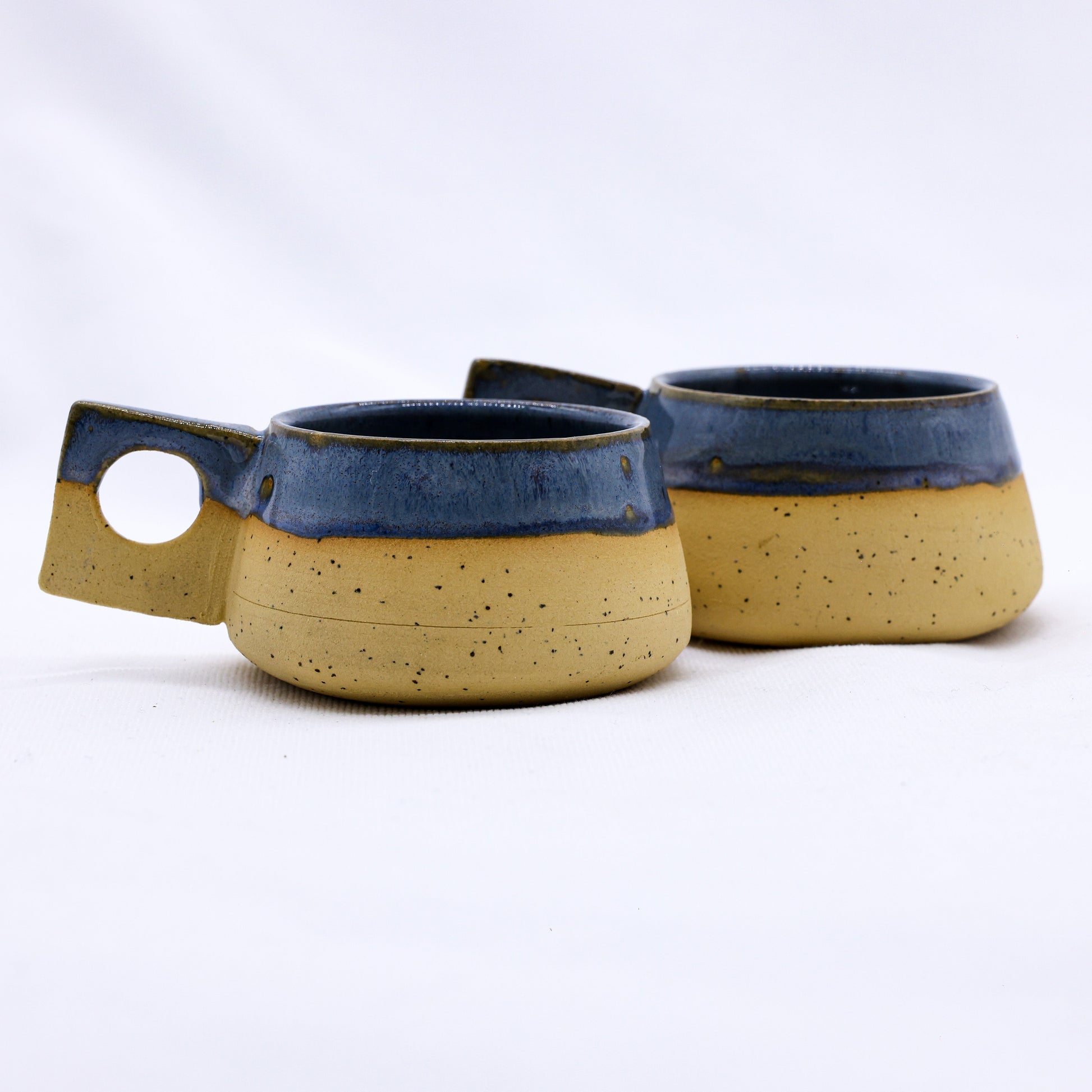 Handmade ceramic mugs with blue glaze and speckled tan base, perfect for van life adventures