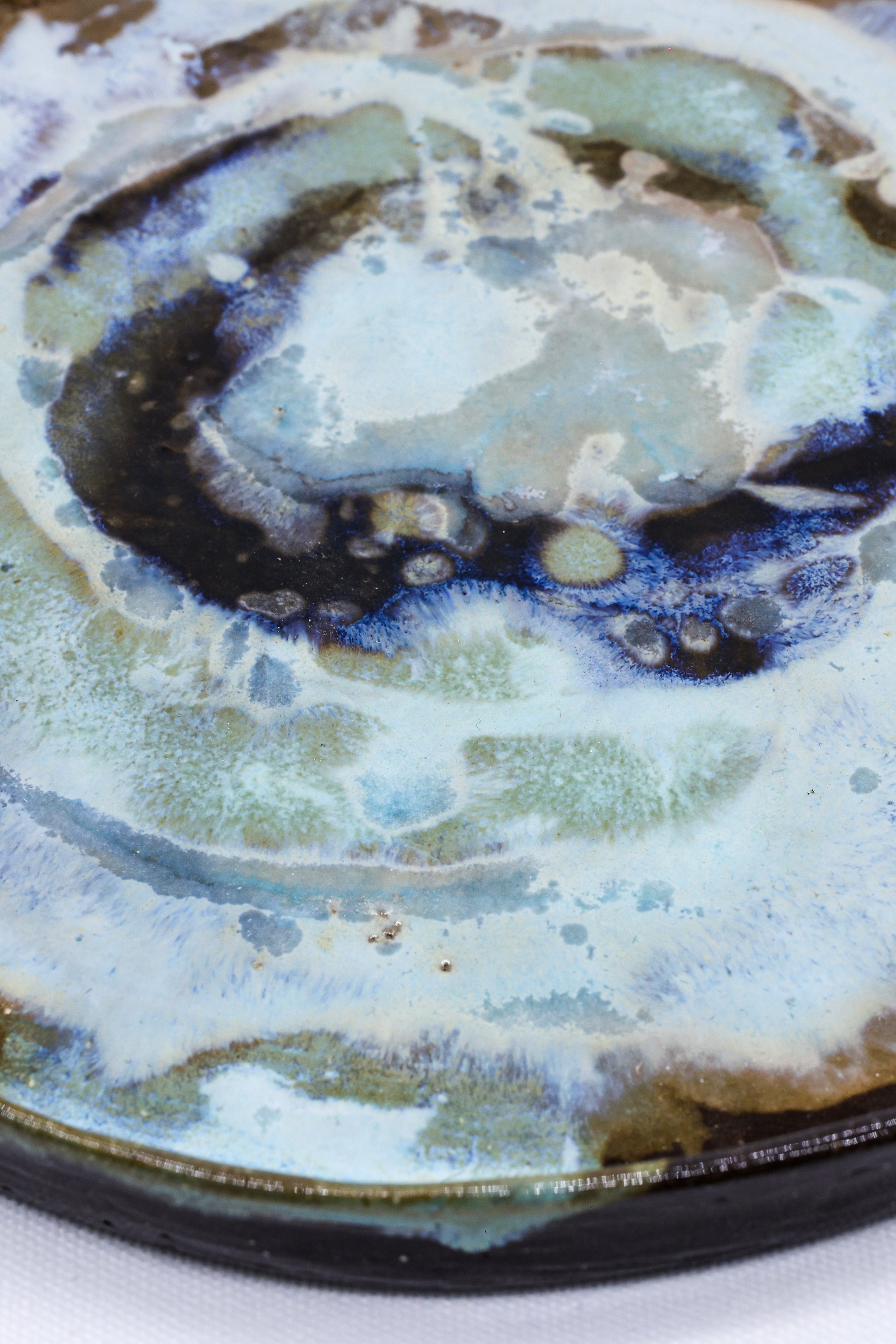 Handcrafted ceramic plate with swirling blue, green, and brown glaze, perfect for van life dining