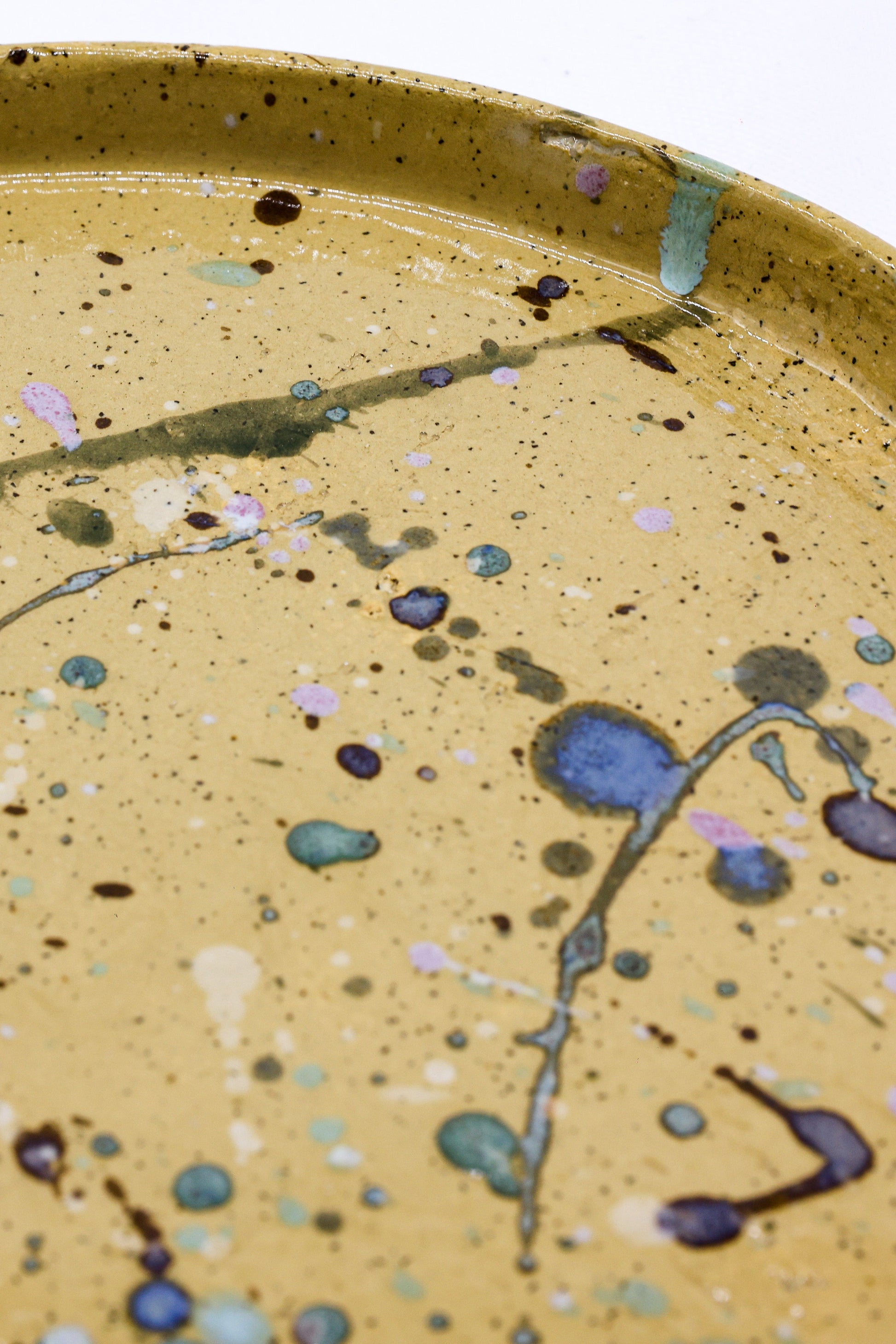 Handmade ceramic plate with speckled glaze and abstract blue, pink, green splatters, perfect for van life dining.
