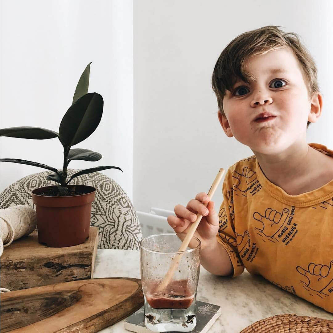 Child sipping smoothie with wooden straw, indoor van life setting with potted plant and rustic decor
