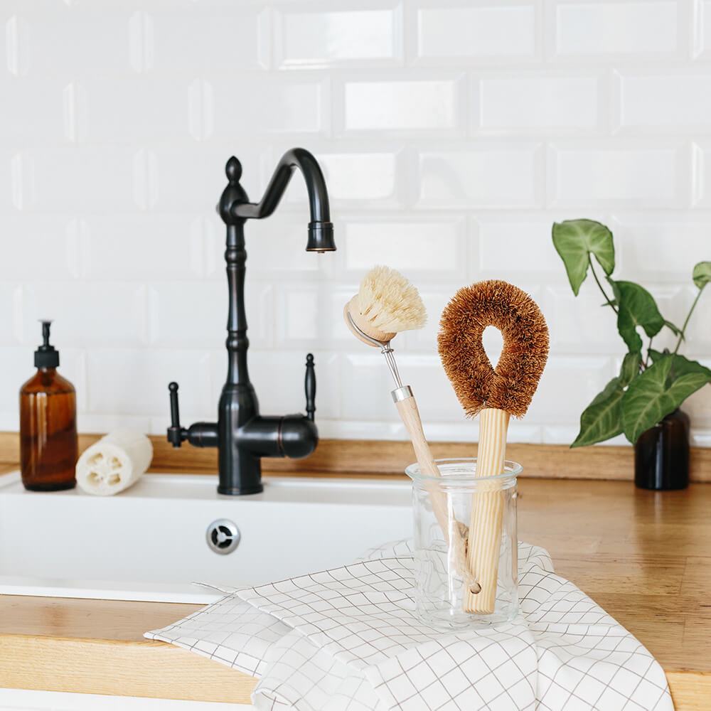 Eco-friendly kitchen brushes in glass jar beside farmhouse sink, van life essentials for compact living
