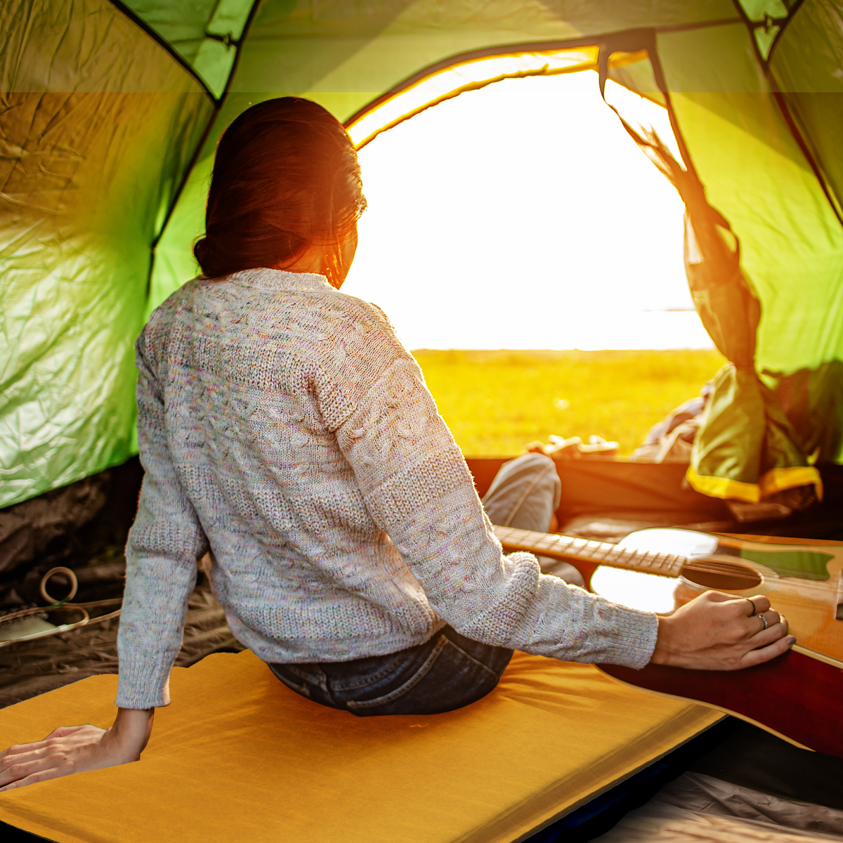 Woman playing guitar inside green tent at sunset, van life camping gear