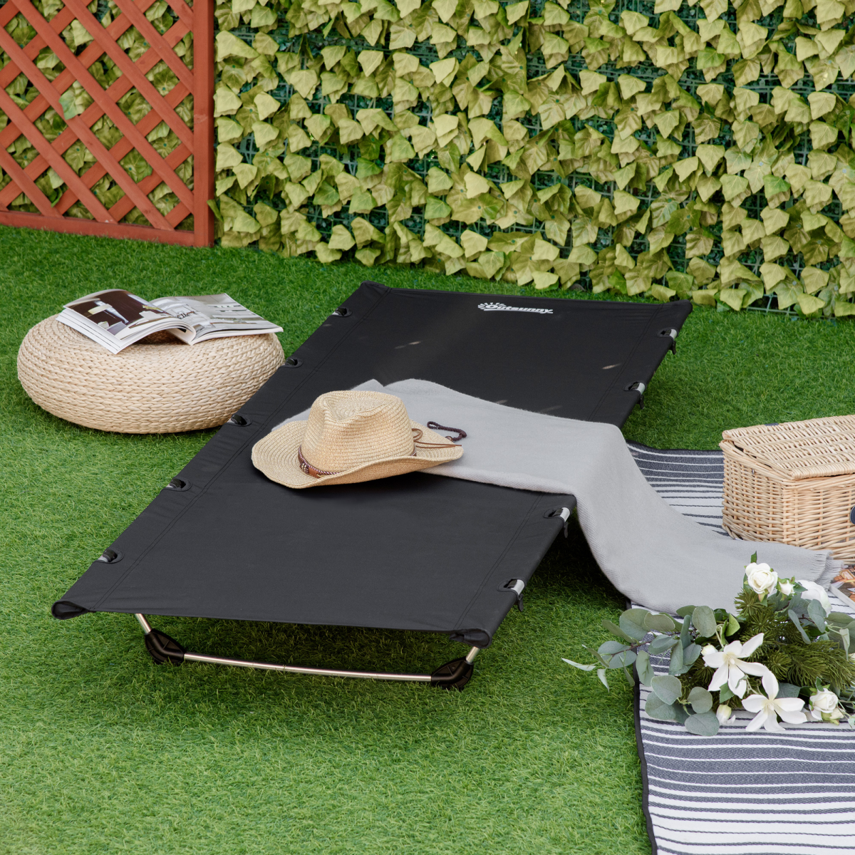 Portable black camping cot with straw hat, blanket, and picnic basket on grass, perfect for van life adventures