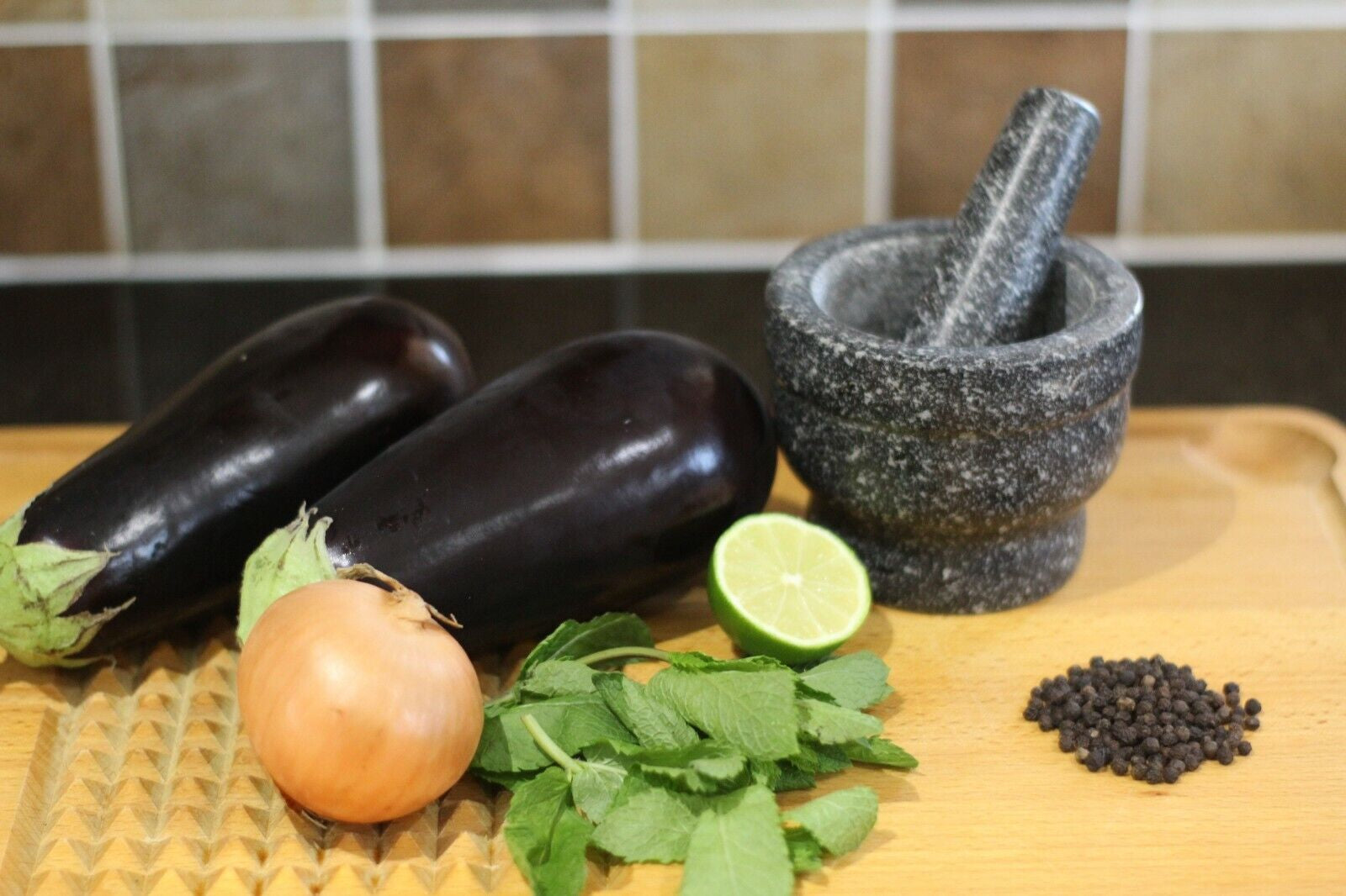 Eggplant, onion, lime, mint, peppercorns, and mortar & pestle on wooden cutting board for van life cooking