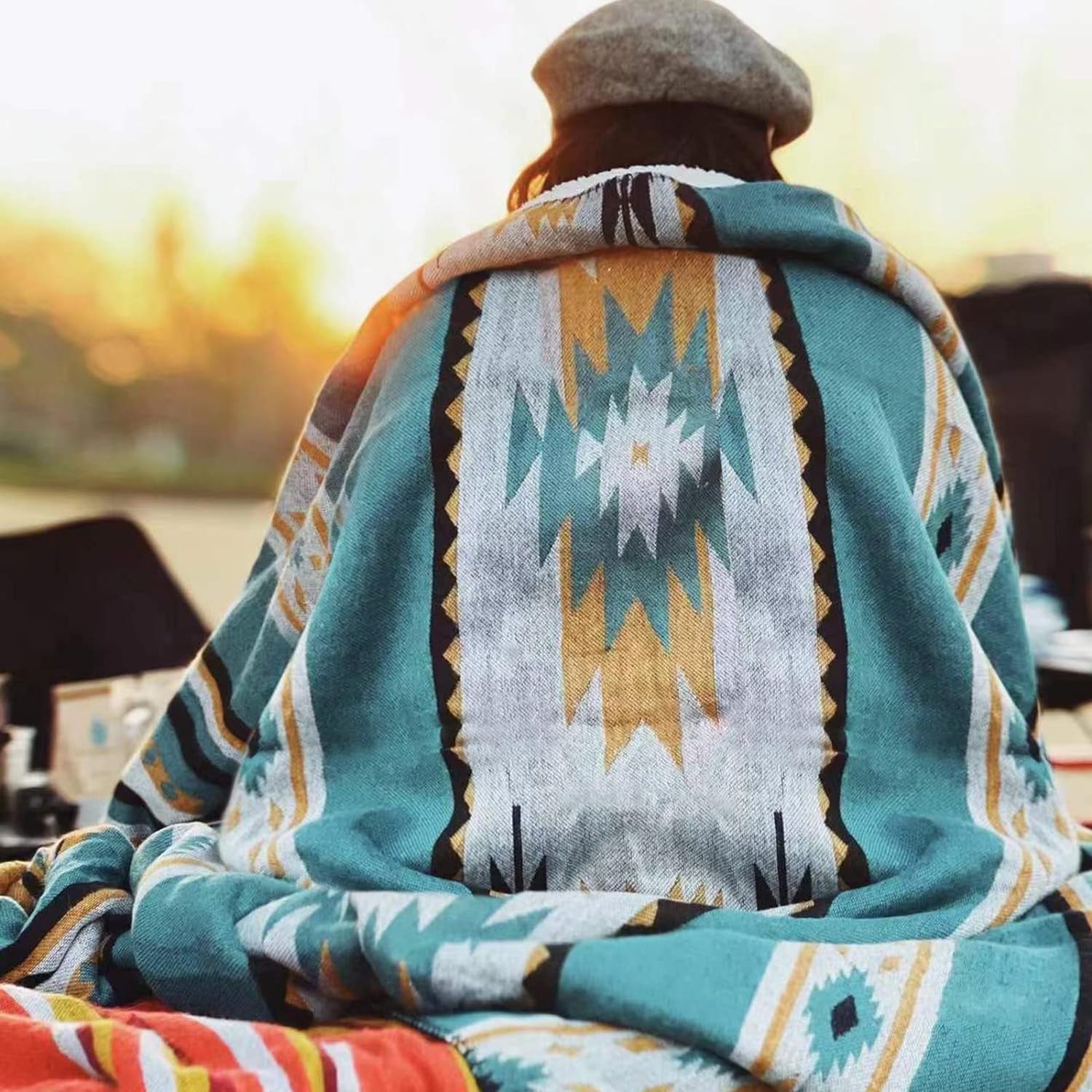 Person wrapped in cozy geometric-patterned blanket at sunset, perfect for van life and outdoor adventures.
