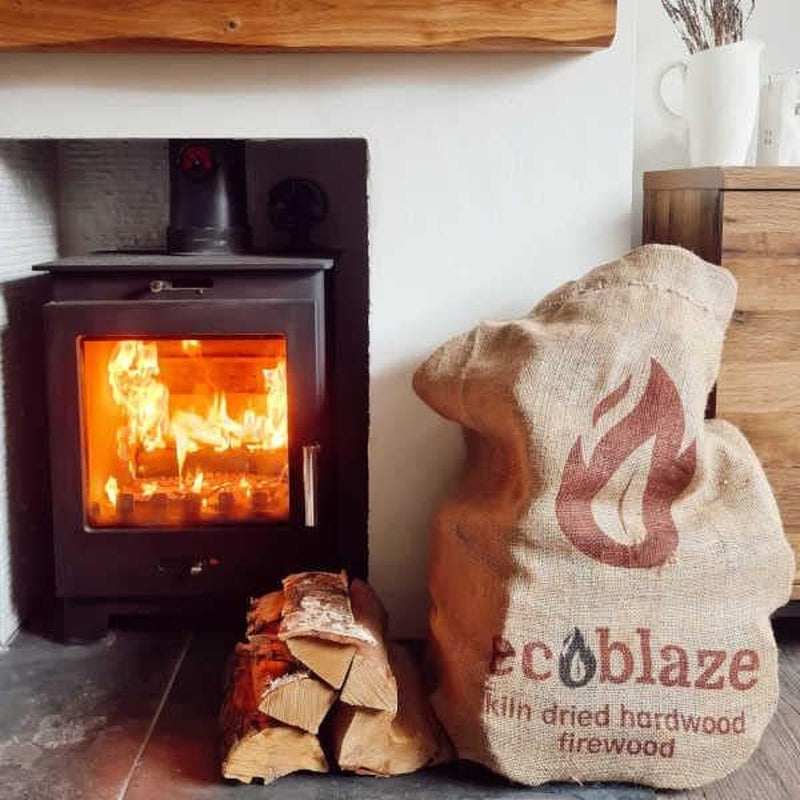 Kiln-Dried Birch Firewood Logs – 50L Hessian Sack – sack and logs beside a wood-burning stove
