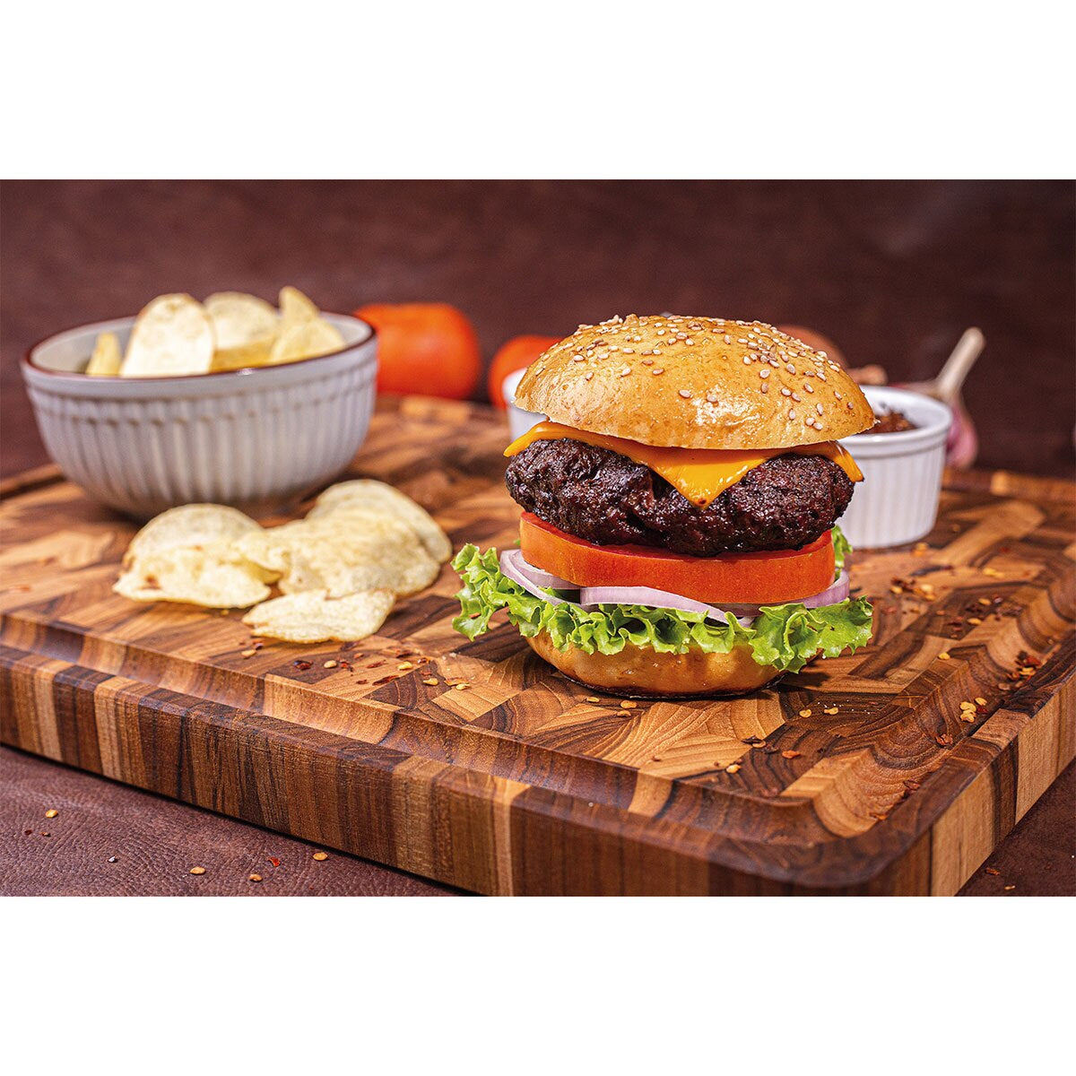 Juicy cheeseburger with lettuce, tomato, onion on wooden board, served with potato chips