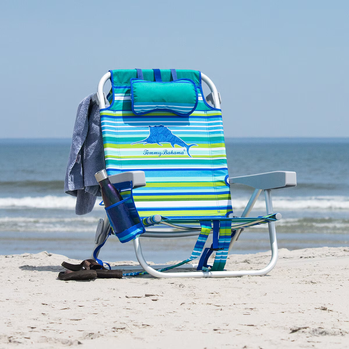 Tommy Bahama beach chair with striped design, cup holder, and towel on sandy shore near ocean