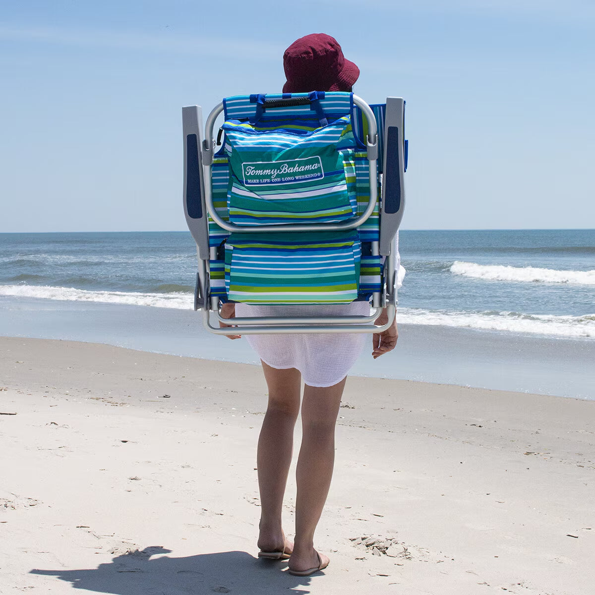 Person carrying Tommy Bahama beach chair on sandy shore, perfect for van life adventures and seaside relaxation.