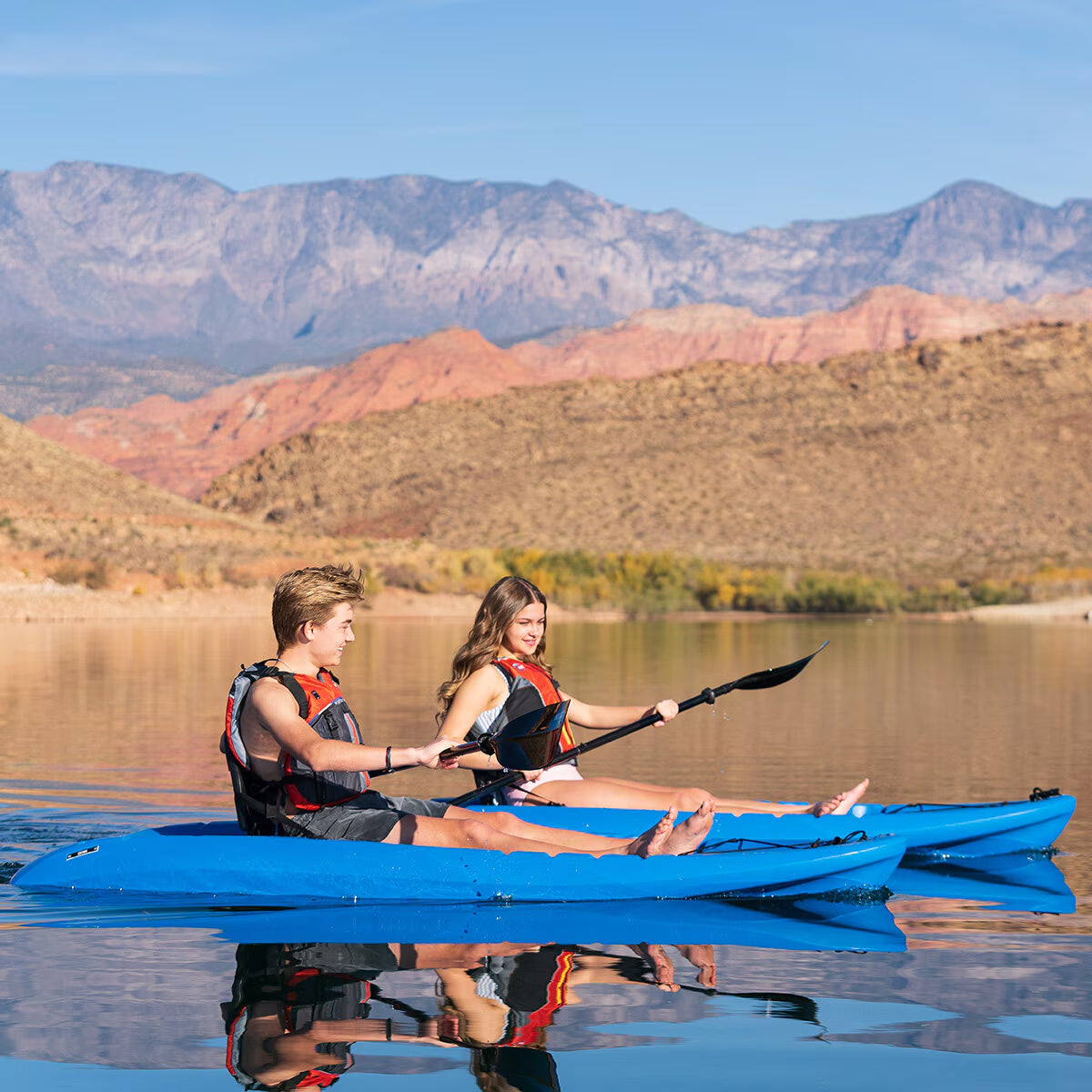 Couple kayaking in blue tandem kayak on calm lake with mountain backdrop, perfect for outdoor adventure gear