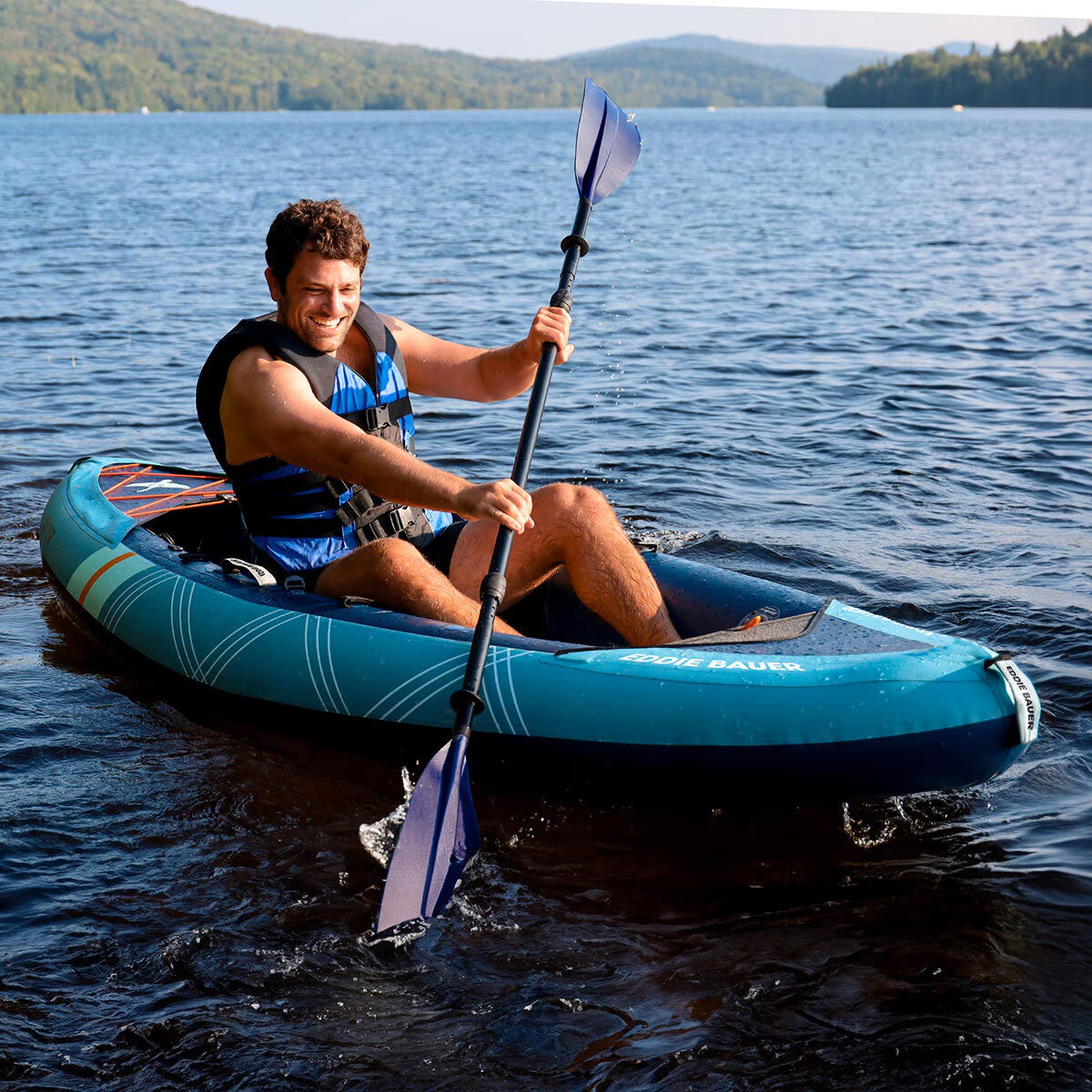 Man paddling blue inflatable kayak on lake, perfect for van life adventures and outdoor exploration.