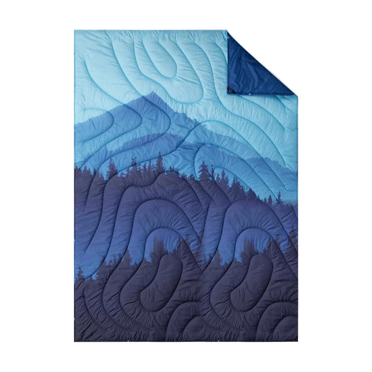 Insulated camping blanket laid flat, quilted with a blue mountain and pine forest print, one corner folded back to show the navy underside