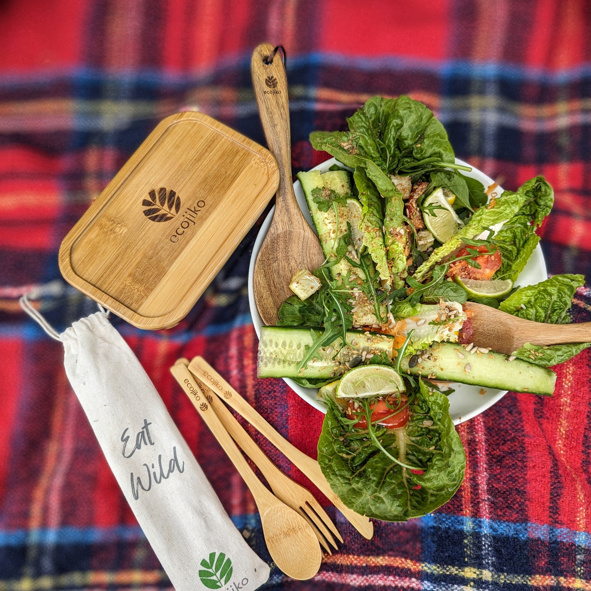 Bamboo salad set with wooden utensils, bowl, and 'Eat Wild' pouch on plaid blanket for van life adventures