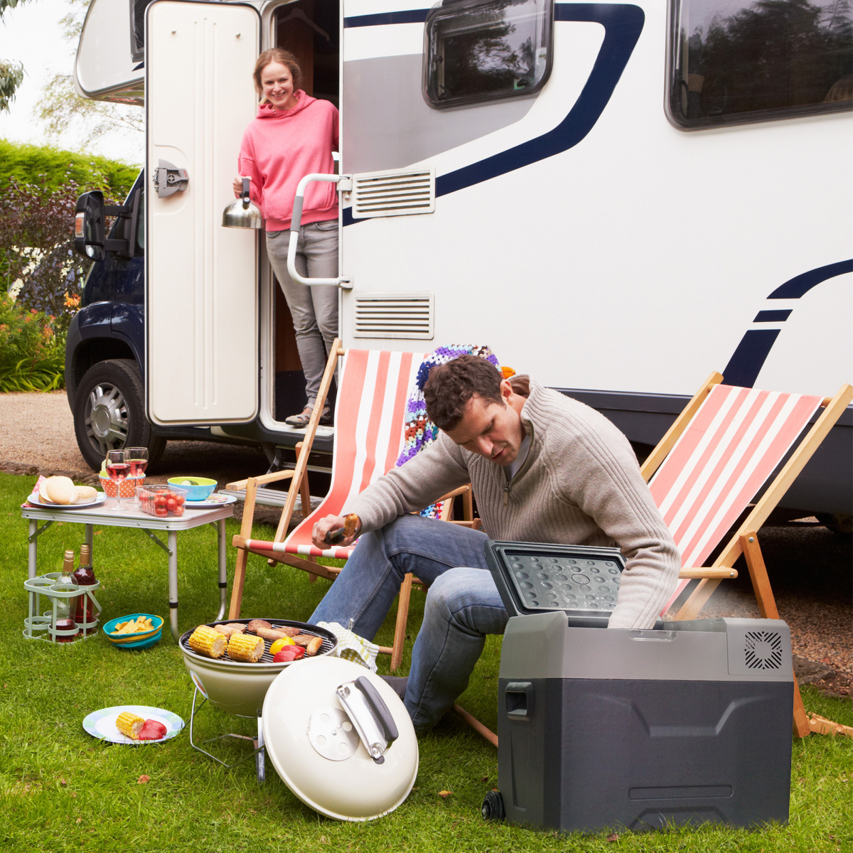 Couple enjoying van life picnic with portable grill, cooler, and camp chairs beside camper van