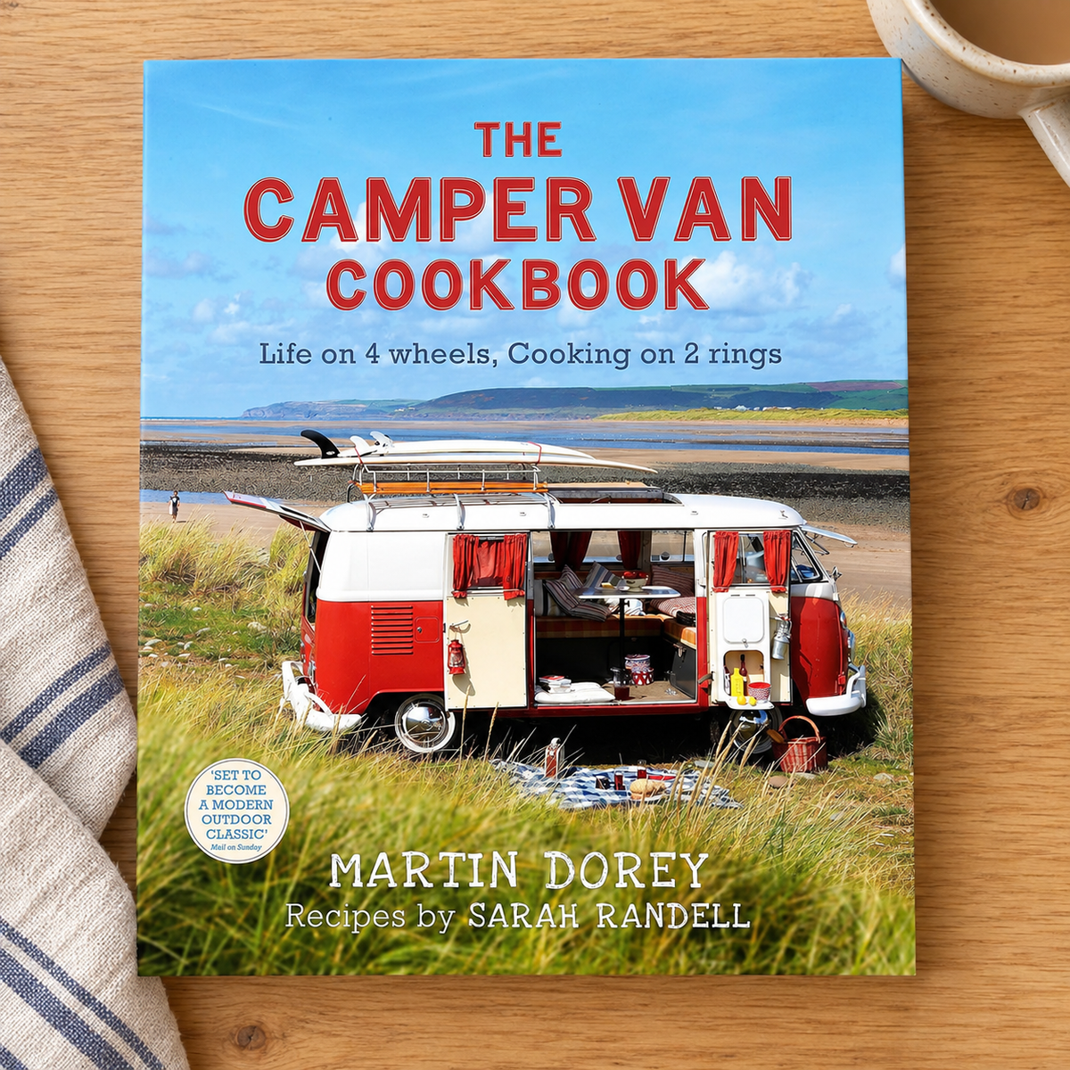 The Camper Van Cookbook: Life on 4 Wheels, Cooking on 2 Rings – book on a wooden campervan table